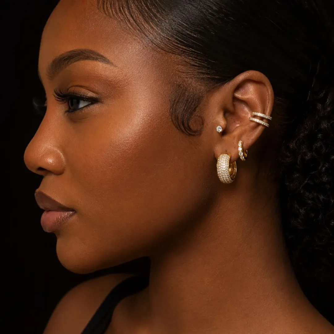 Model in profile wearing Saint Collection gold huggie hoops, ear cuff and stud earrings